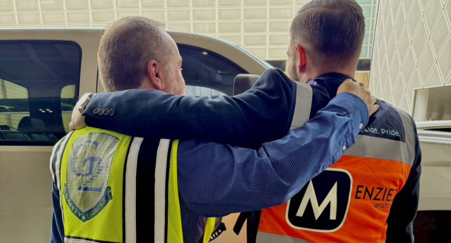 To colleagues hug whilst wearing Menzies and G2 high visibility vests.