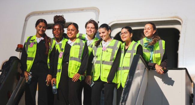 The students smile for a photo at the top of the passenger boarding stairs. The students smile for a photo at the top of the passenger boarding stairs.