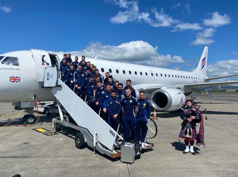 Scotland football men's team on plan steps with a bagpiper