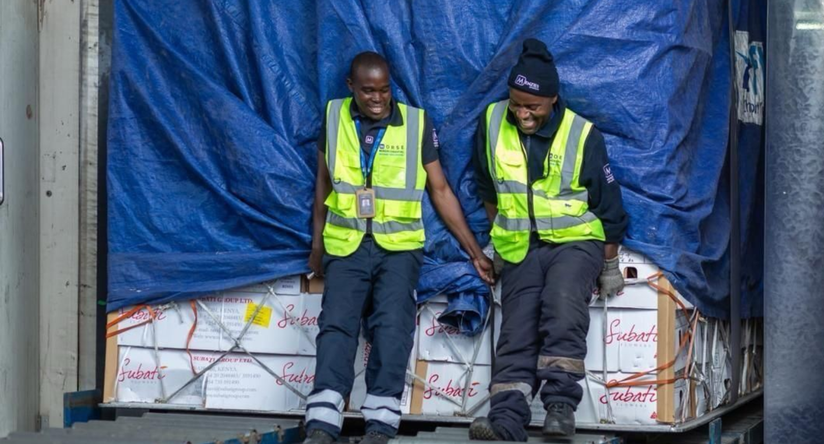 Colleagues in Kenya smile in front of a cargo shipment