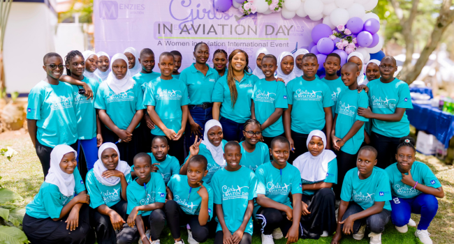 The girls gather for a group photo in front of a Girls in Aviation Day board and balloons.